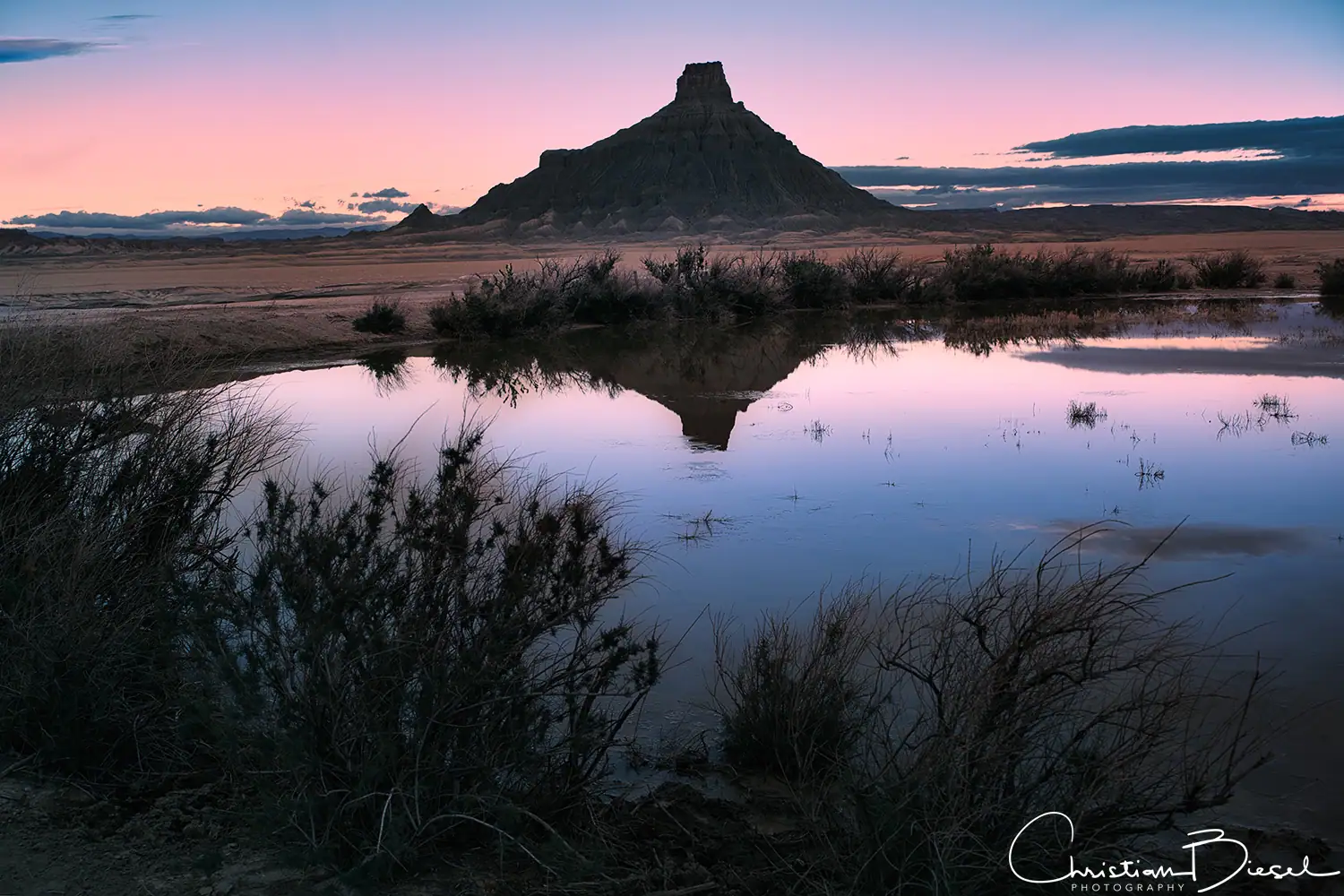 Spiegelung am markanten Factory Butte vor Sonnenaufgang. Reflexion des Factory Butte im Wasser vor Sonnenaufgang, beeindruckende Szenerie mit rötlichem Himmel.