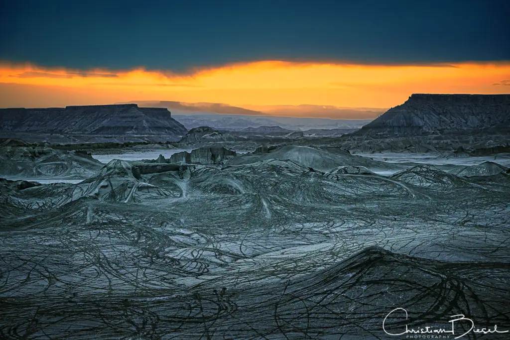 Aussicht auf die Swing Arm City, Utah mit beeindruckenden Felsen der North und South Caineville Mesa und einem dramatischen Sonnenuntergang am Horizont.