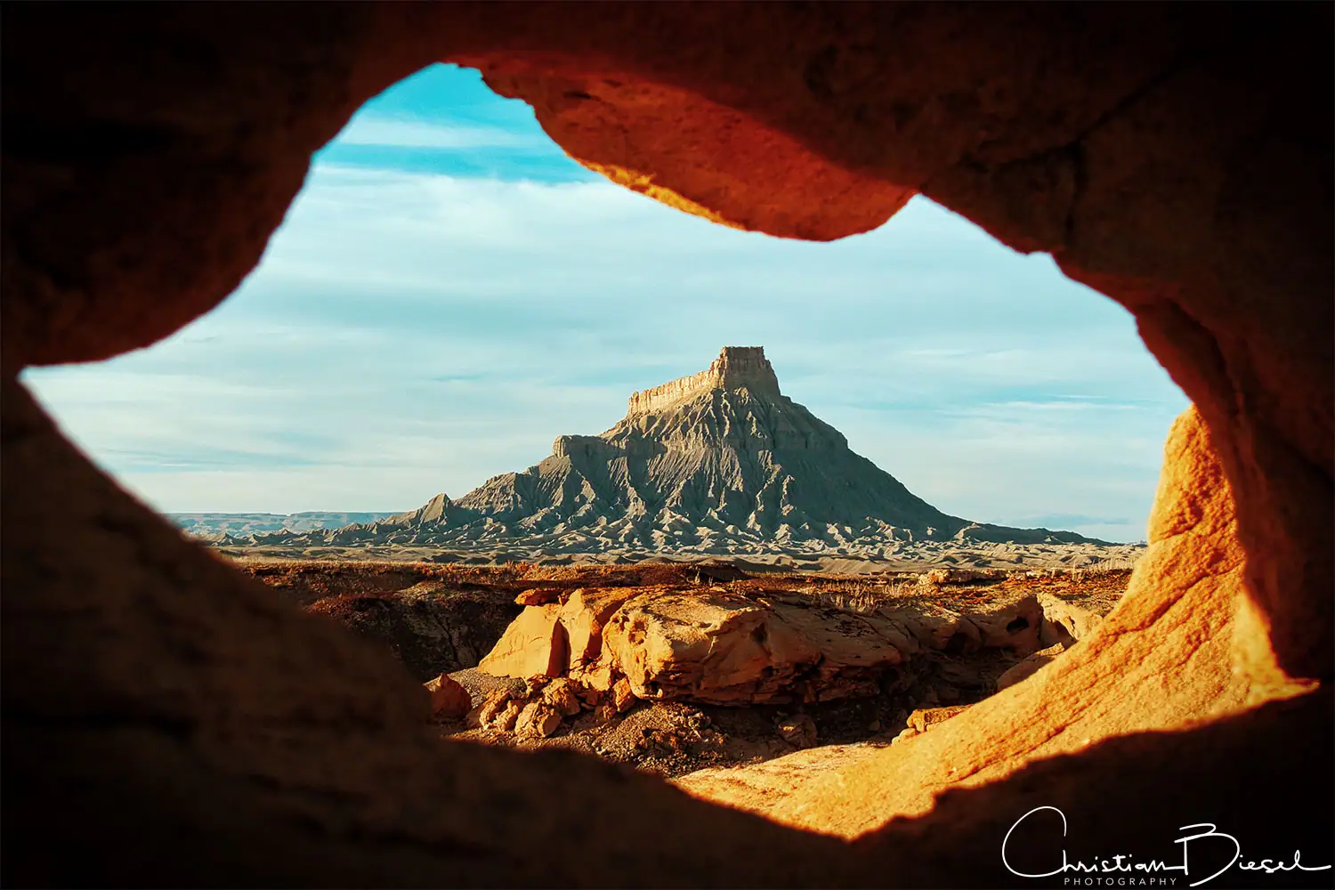 Factory Butte, gesehen durch natürliche Felsöffnung. Fotografie des Factory Butte im Südwesten der USA, Blick durch einen roten Felsen.