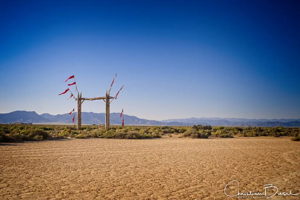"Entrance to Namaajin" - weit sichtbare Zufahrt zu Outpost X bei Beryl, Utah, mit Holztor und mehreren Fahnen